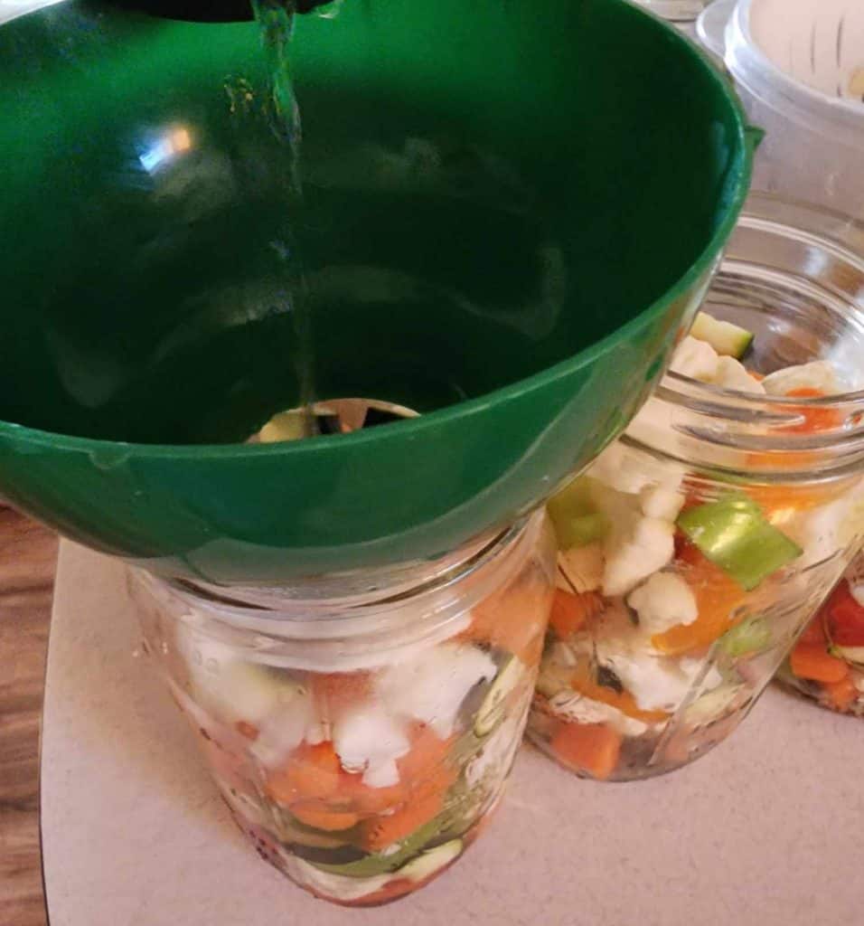 Adding brine to the jars of mixed vegetable for canning pickled giardiniera