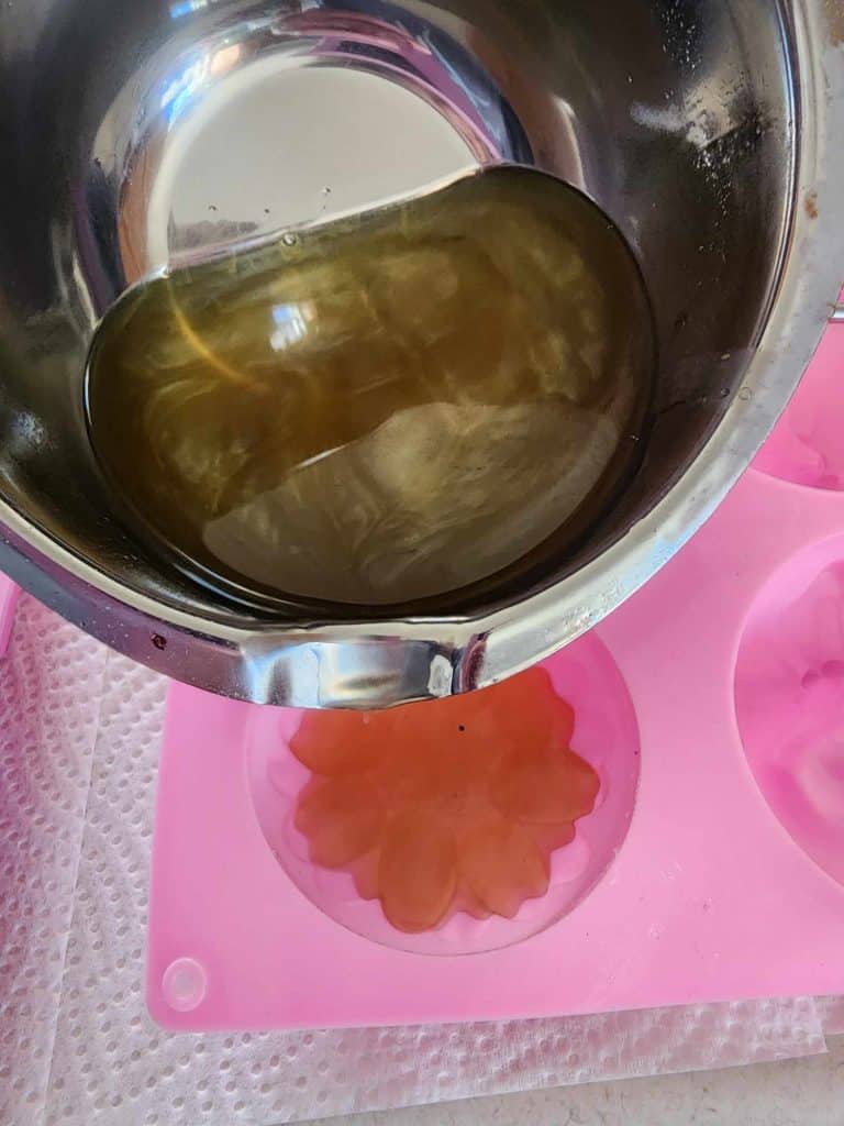 pouring rosemary infused oil mixture into silicone molds to make rosemary lotion bars