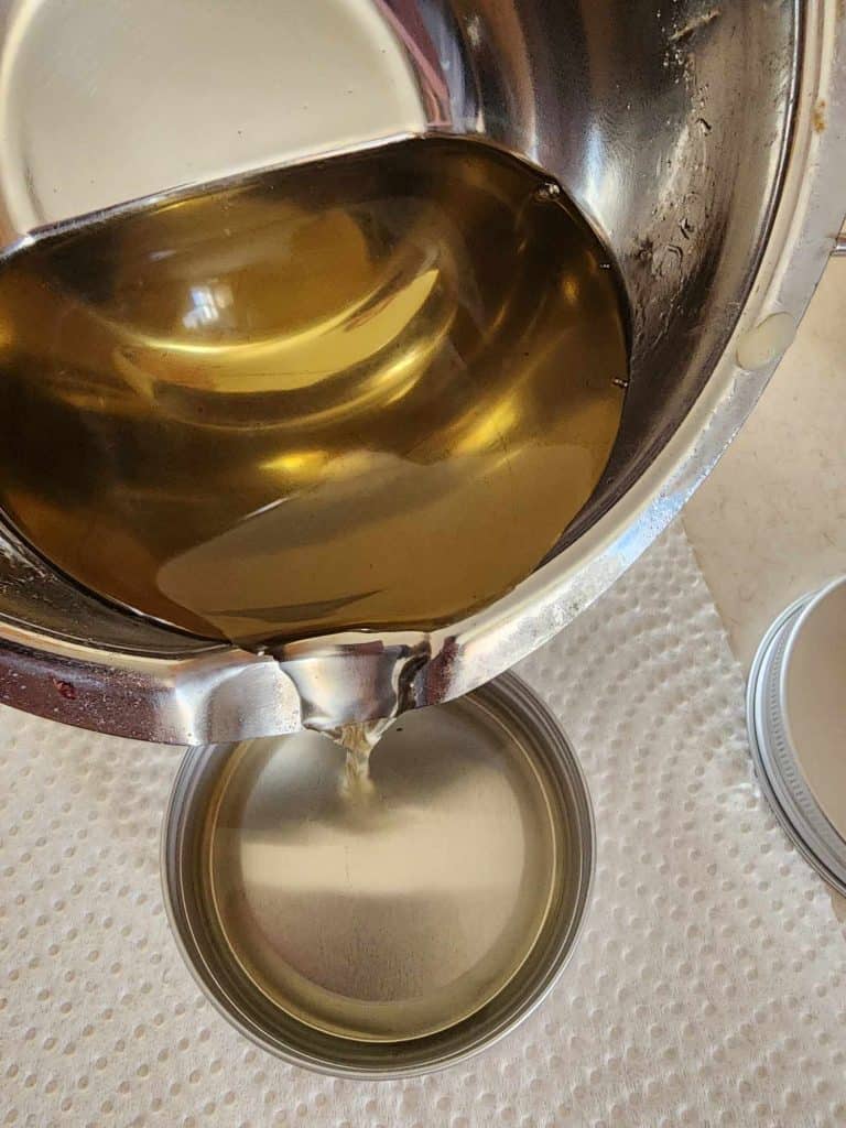 pouring infused oil mixture into tins to make rosemary salve