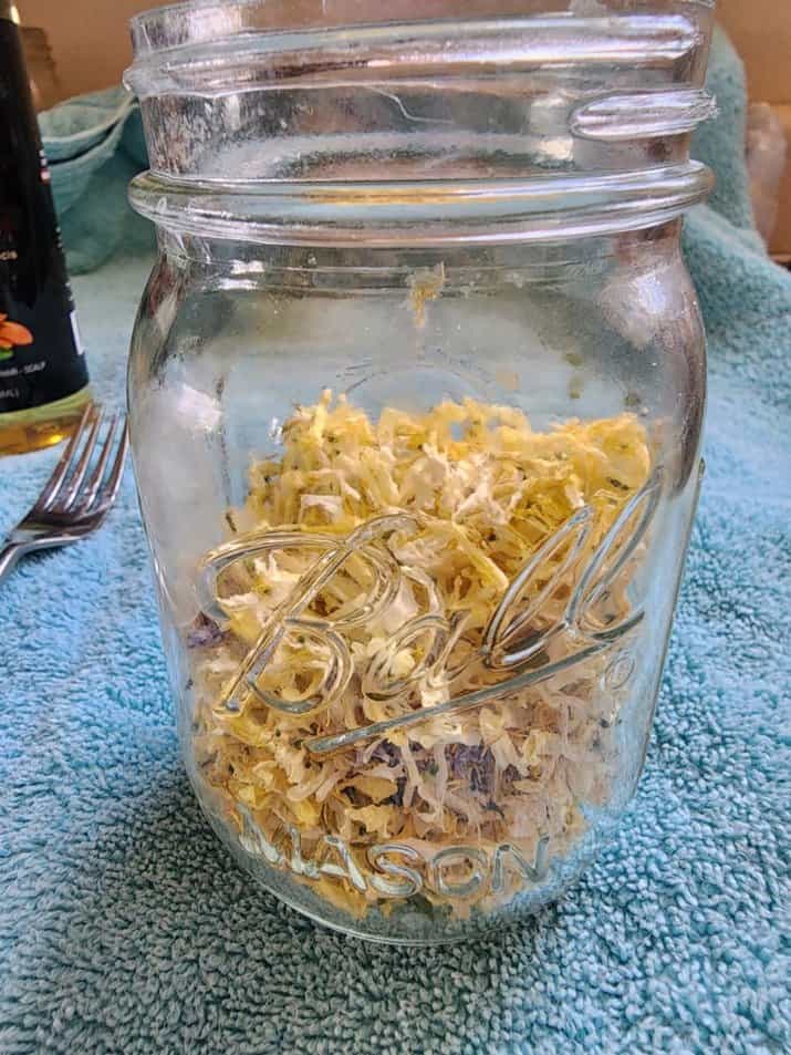 Adding dried honeysuckle to a mason jar to make honeysuckle salve