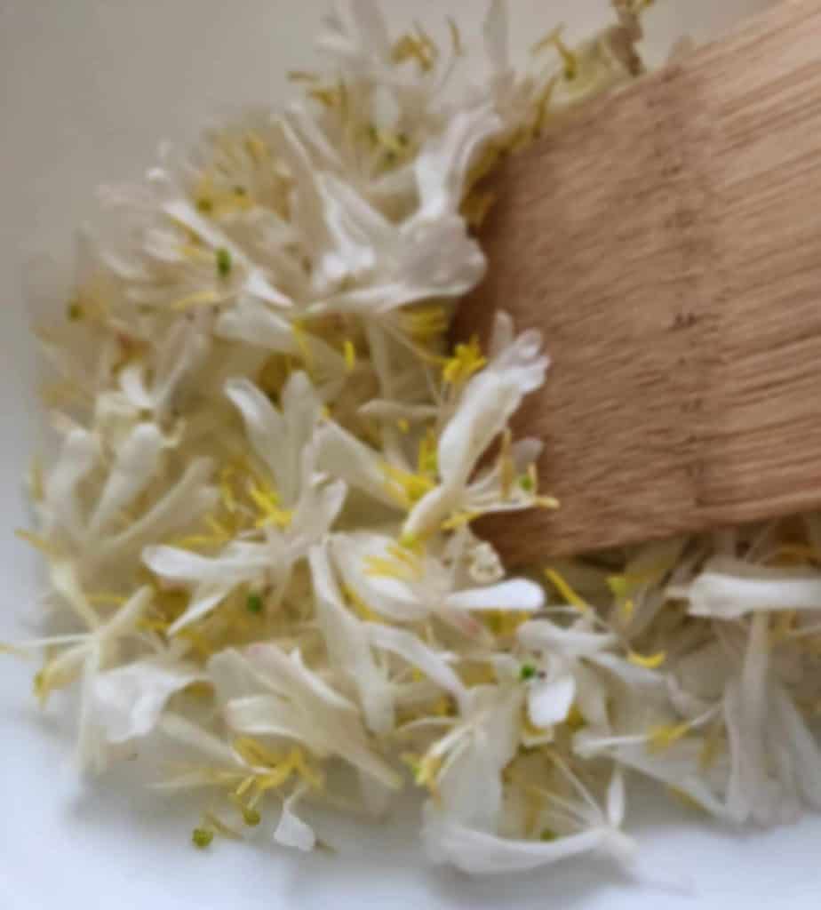 Bruising the honeysuckle flowers with a wooden spatula for honeysuckle tea