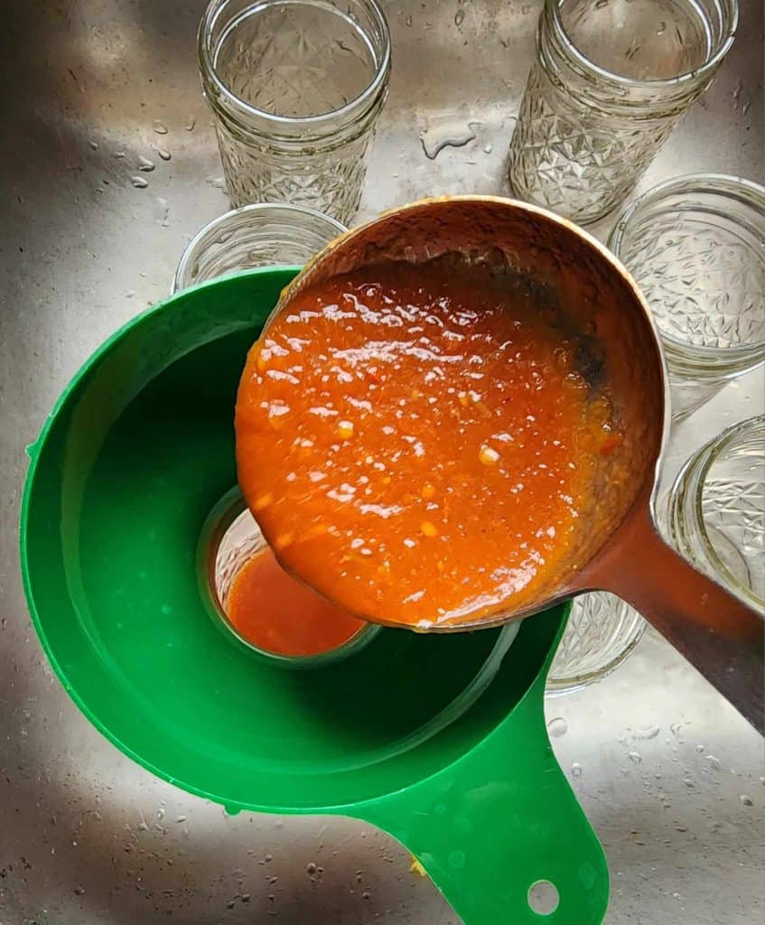 ladling homemade bbq sauce into the canning jars