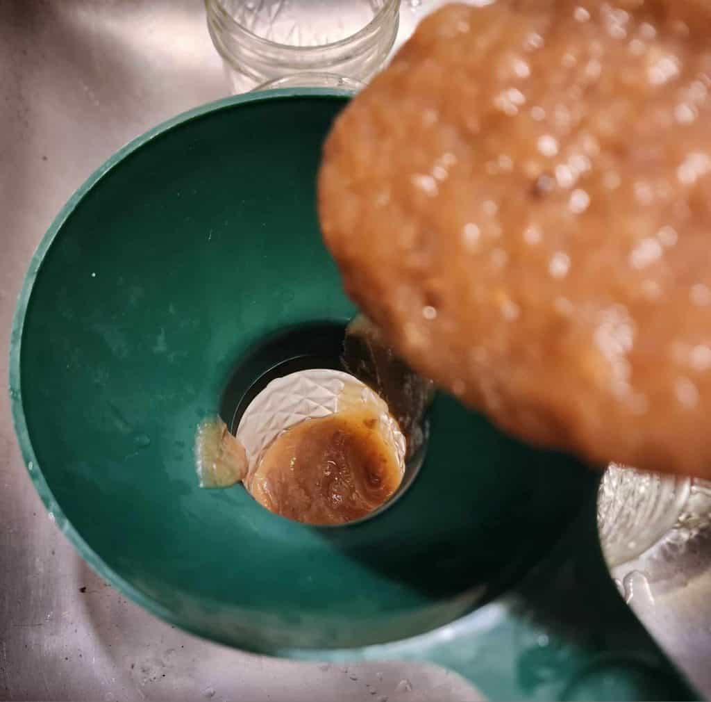 ladling apple jalapeno bourbon bbq sauce into jars
