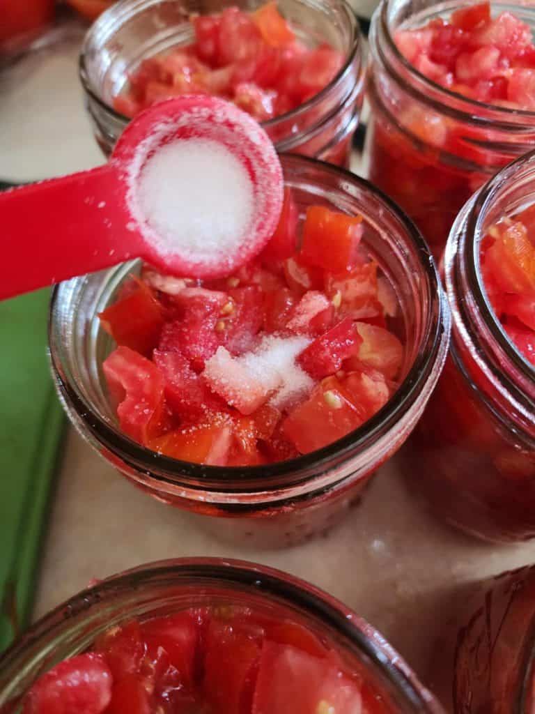 adding salt to jars of diced tomatoes