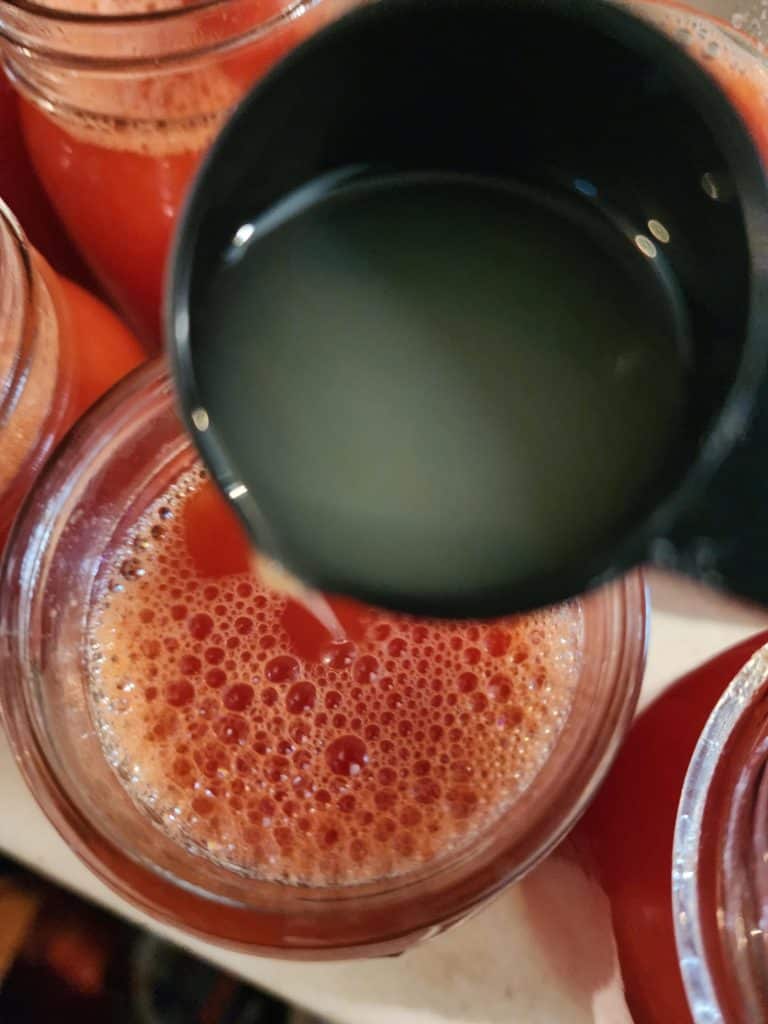 adding lemon juice to the jars of tomato juice for canning