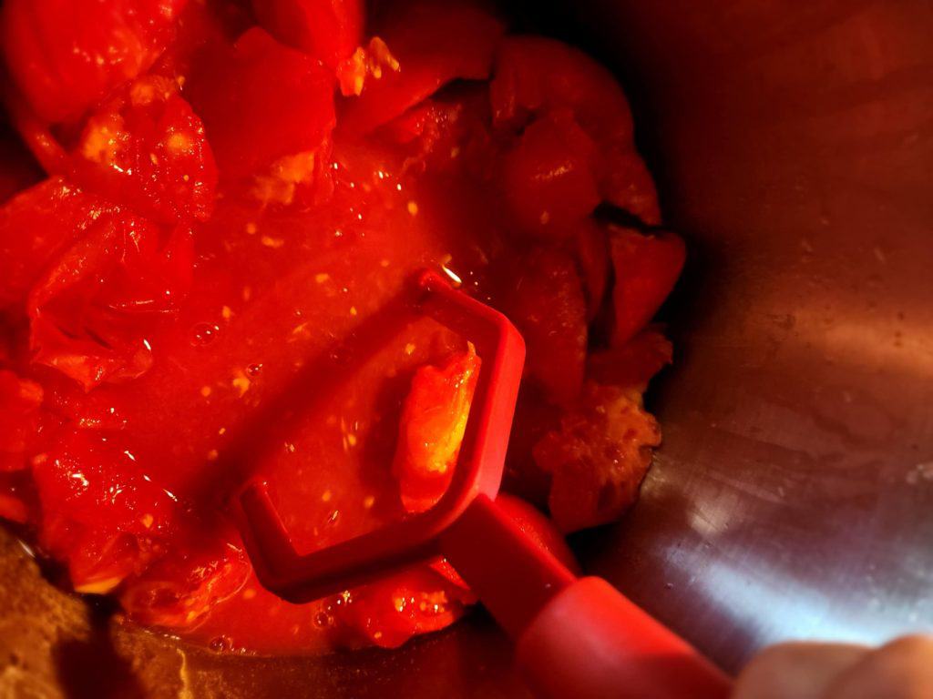 mashing cut up tomatoes while simmering with potato masher to make tomato juice