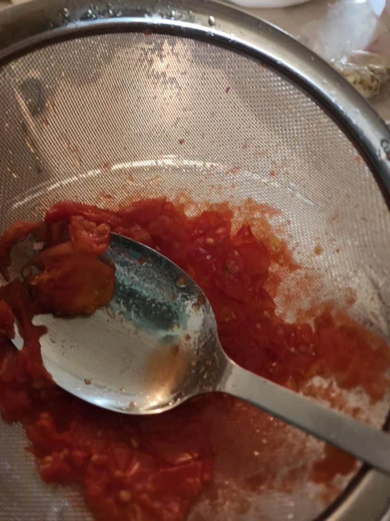 pushing juice out of tomatoes with a strainer and spoon