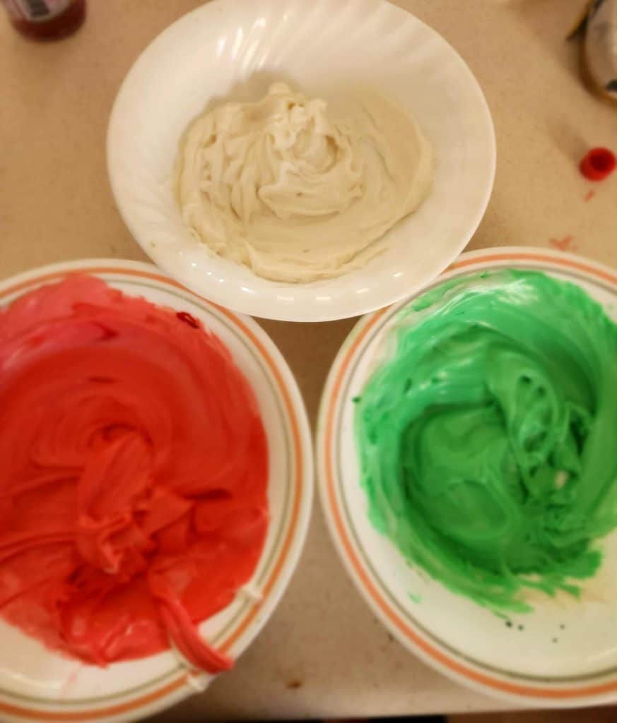 bowls of frosting dyed red and green, plus one white bowl for Christmas cake