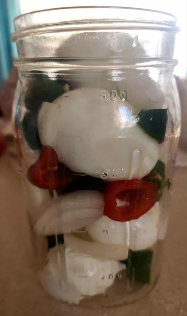 hard boiled eggs layered with hot peppers and onions to make sweet and spicy pickled eggs