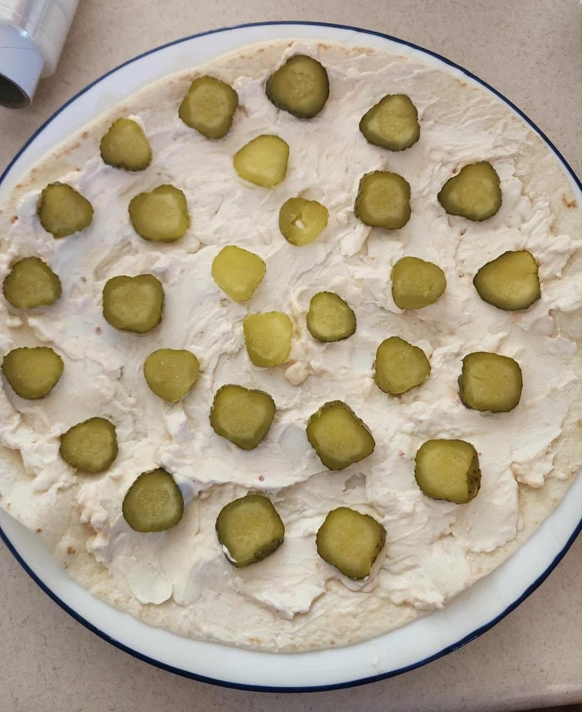 Baby dill pickle slices placed on tortilla for salami pickle roll ups