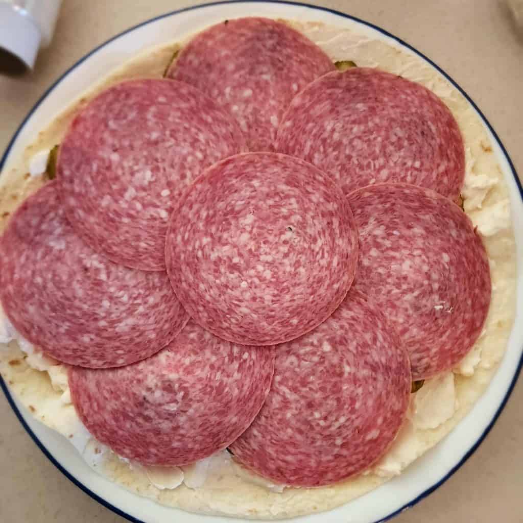salami slices placed on top of the tortilla to make salami pickle roll ups
