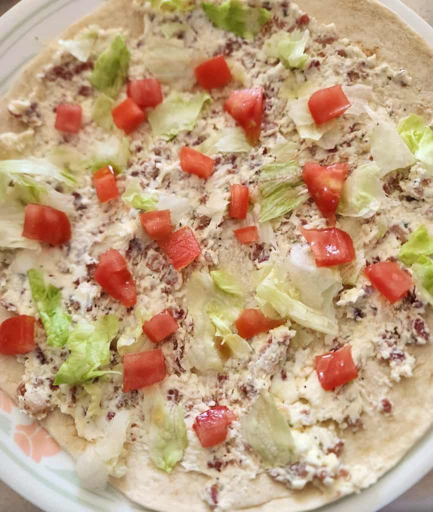Lettuce and tomato placed on BLT cream cheese mixture to make BLT roll ups